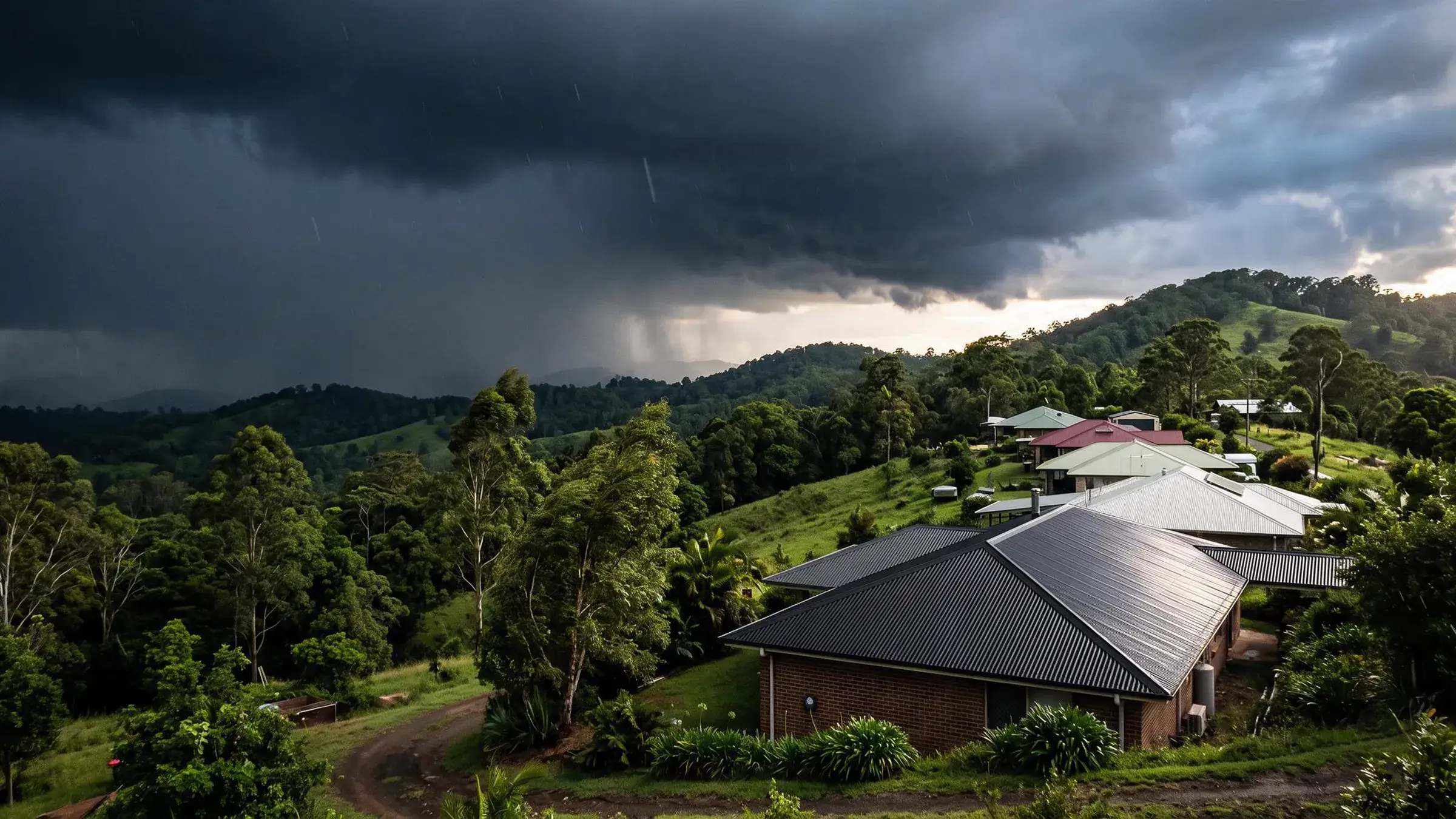 Illustrative image of storm clouds building over metal-roofed homes on a green hinterland ridge