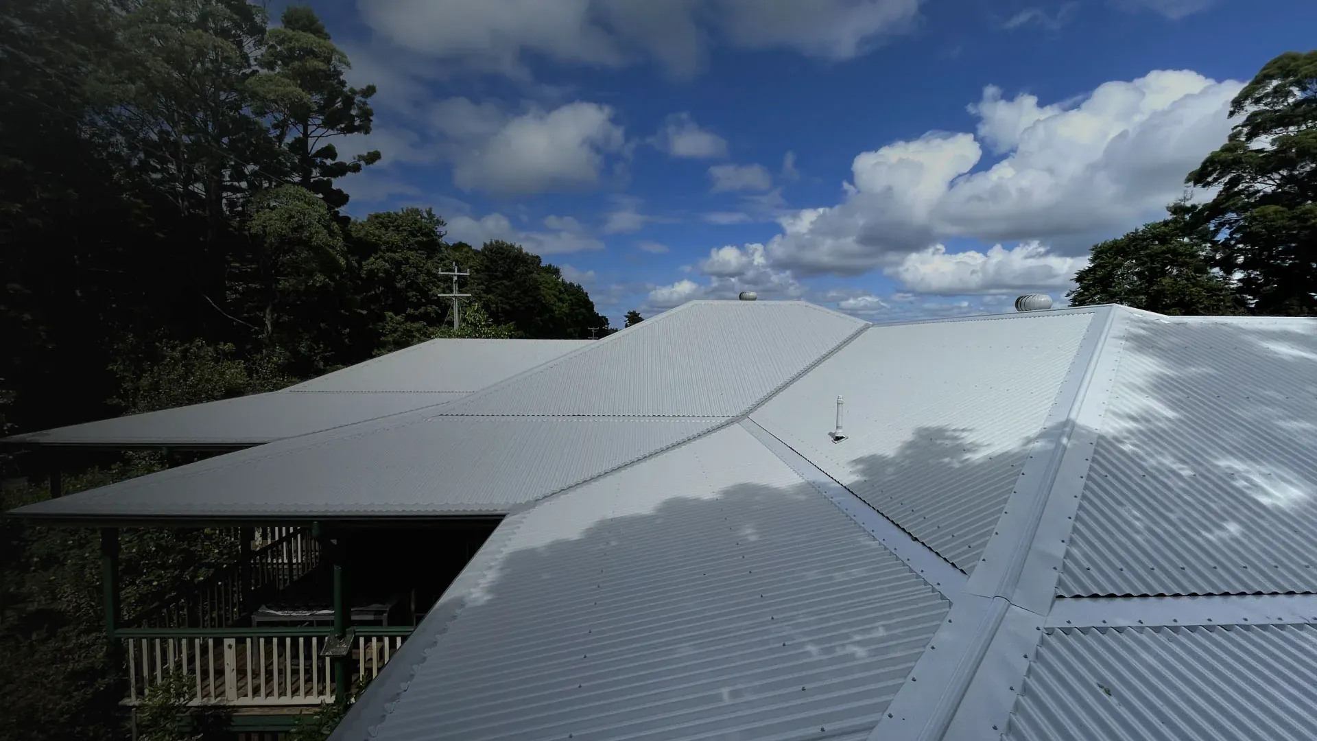 Light grey corrugated roof with hip and valley cappings, two whirlybirds and a vent pipe flashing above a timber verandah