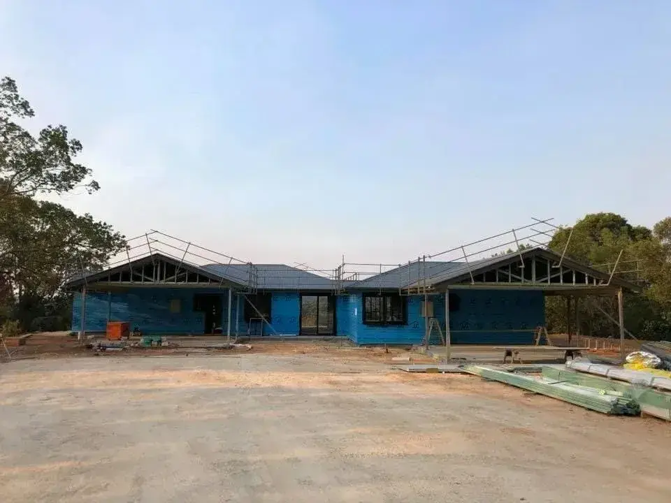 New home frame with roof trusses, scaffold edge protection and packs of roof sheets on the ground ready to install