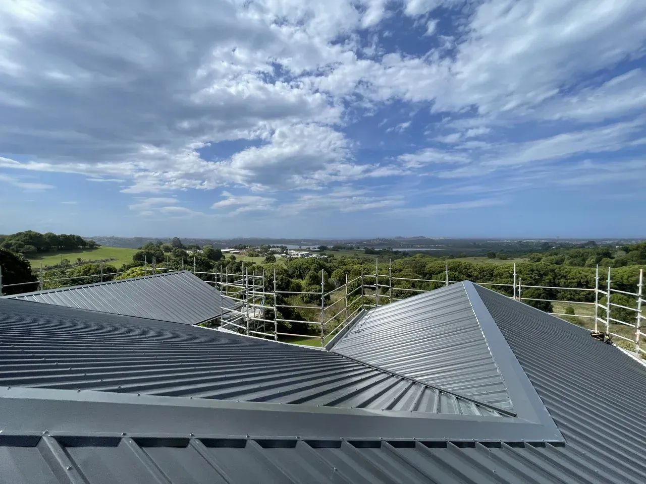 Dark ribbed metal roof with scaffold edge protection looking out over green hinterland towards the coast