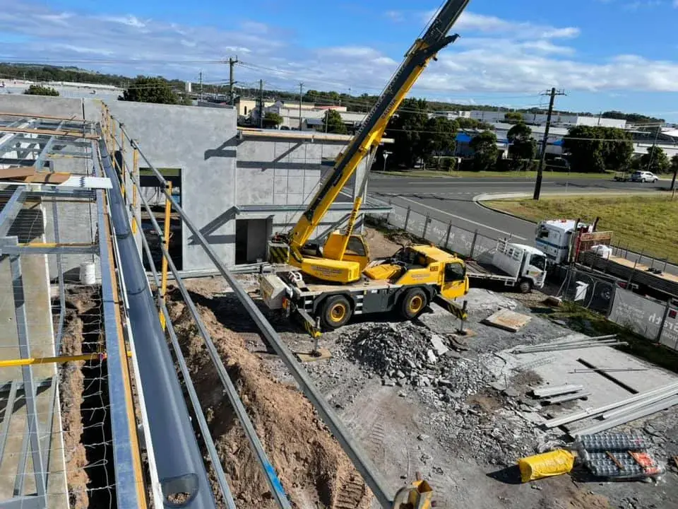 Crane lifting roofing materials onto a commercial building site, with a new gutter run in the foreground