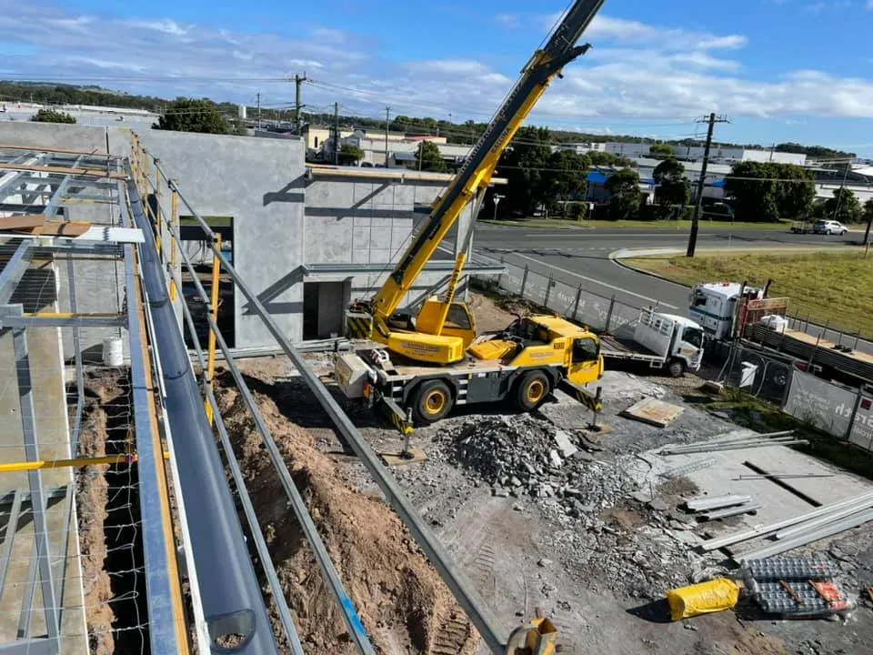 Crane lifting roofing materials onto a commercial building site, with a new gutter run in the foreground