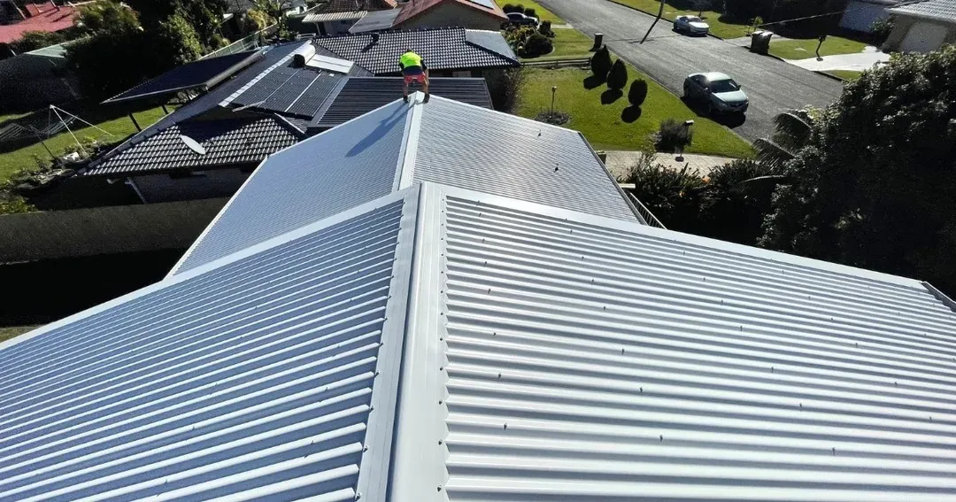 New light metal roof with a worker on the ridge, surrounded by tiled neighbouring roofs and solar panels
