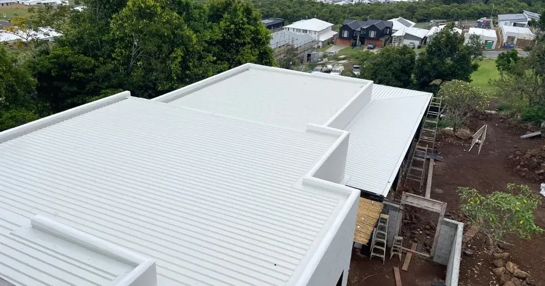 Low-pitch light-coloured metal roof on a new home above red soil