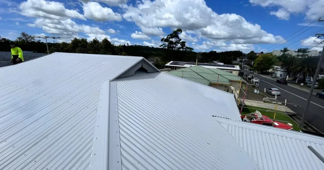 Roofer in hi-vis on a light-coloured metal roof above a suburban street