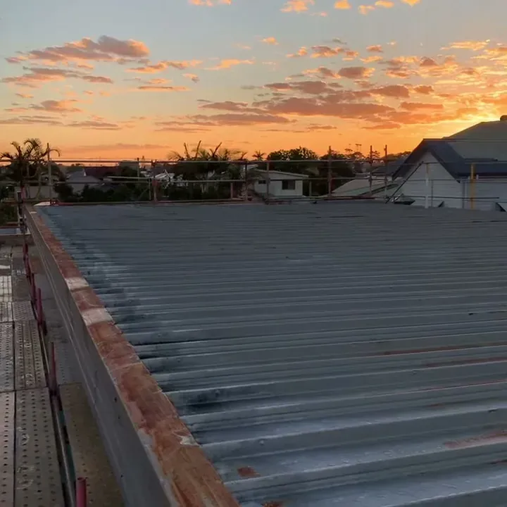 Sunrise over a rusted clip-lock roof with a scaffold walkway before replacement in Ballina